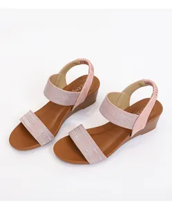 Detailed macro view of pink glitter strap and brown wedge sole of women's roman sandals