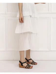 Detalle de sandalias de cuña negras con tachuelas doradas y falda plisada blanca