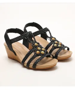 Detalle de tiras tejidas negras con cuentas turquesas y cuña con acabado de veta de madera