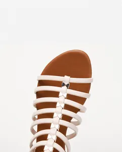Detail of cream white leather sandals featuring multiple straps with gold bow accents
