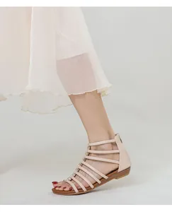 Side view of beige wedge sandals with metallic buckles and zipper heel on a model