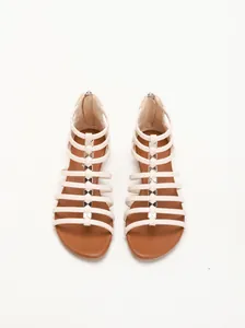 Detail of wedge sandals with thin beige straps, metal bow charms and back zipper closure