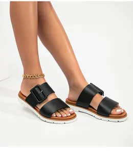 Détail de sandales à double bride noire avec grandes boucles et semelle blanche antidérapante
