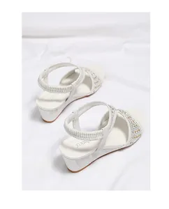 Detail of white wedge sandals featuring crisscross straps with gold studs and elastic heel
