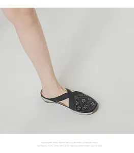 Detail of women's black flat mules with criss-cross straps, hollow patterns and rhinestones