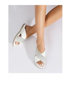 Detalle de las correas cruzadas de cuero blanco y strass plateado en sandalias planas de mujer