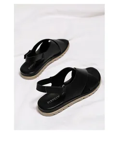 Detail of black leather cross-strap sandals with adjustable metal buckle and thick sole