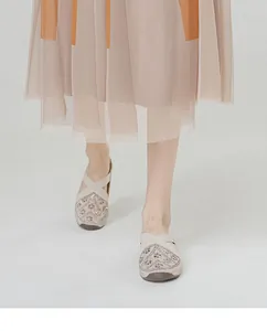 Close-up of beige slip-on shoes with geometric floral patterns and crystal accents