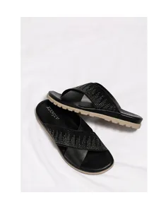 Detalle de sandalias planas negras con tiras cruzadas de pedrería y cuero de alta calidad