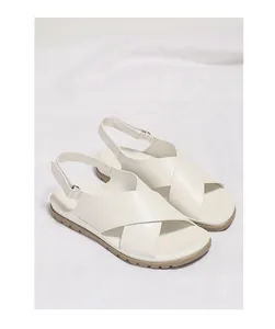 Detail view of white criss-cross strap sandals with non-slip rubber soles on white linen