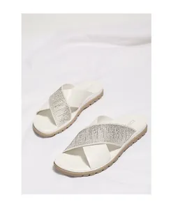 Detalle de sandalias blancas con tiras cruzadas, pedrería plateada y suela marrón