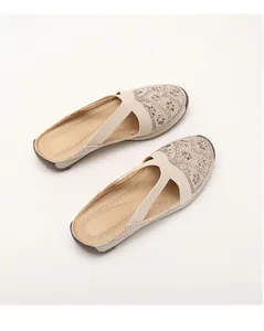 Close-up of beige mule flats featuring rhinestone flower details and elastic cross straps