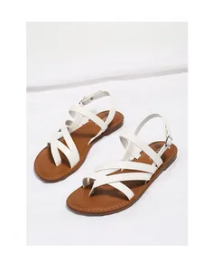 Detail of white cross-strap flat sandals with adjustable buckles and brown leather insoles