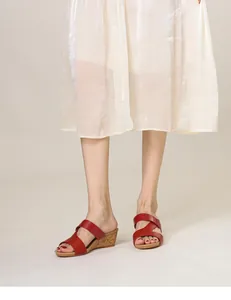 Détail de sandales compensées en cuir rouge avec talon en liège portées avec robe plissée