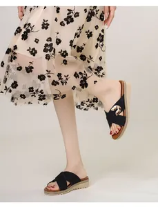 Detail of black wedge flip-flops with wide crossover straps and gold metal ornament