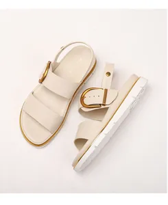 Nahaufnahme cremefarbener Modesandalen mit goldener Hufeisenschnalle und Plateausohle