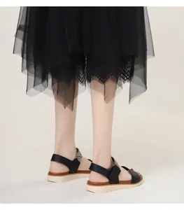 Detail view of black wedge roman sandals with woven heel and elegant layered lace skirt