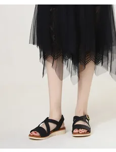Detail of black cross-strap sandals with gold buckle and textured platform sole on foot