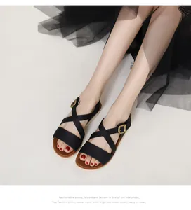 Close-up of black cross strap wedge sandals with gold buckle detail on a model
