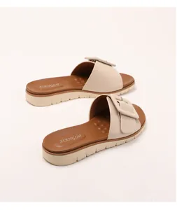 Detalle de sandalias de cuña beige con hebilla cuadrada decorativa y suela con textura