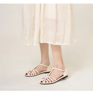 Detailed view of woven cut-out flat sandals in creamy beige on feet with t-strap buckle