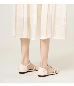 Close-up of beige woven flat sandals with ankle buckle strap styled with white skirt