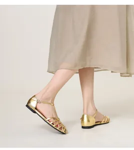 Close-up of golden woven hollow flat sandals with T-strap and buckle closure for women