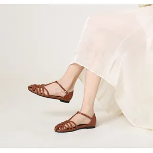 Detail of brown woven hollow-out flat sandals with T-strap and buckle on feet