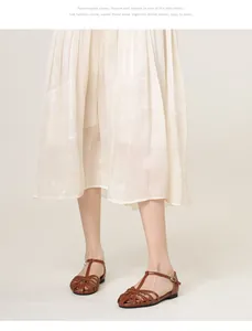 Detailed view of brown woven leather flat sandals with T-strap buckle and pleated skirt