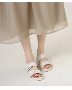 Close-up of cream double buckle slides paired with a pleated skirt for a casual summer look