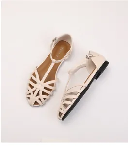 Detailed view of beige woven flat sandals with hollowed design and metal buckle closure