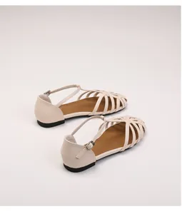 Detail of hollow-out beige woven sandal with ankle buckle and black anti-slip flat sole