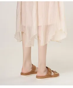 Close-up of brown platform slide sandals with double buckles worn with a pleated skirt