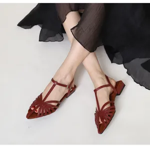 Detailed view of woven dark red low-heel Roman sandals on model with adjustable straps