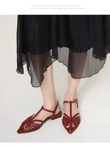 Macro shot of red T-strap pointed toe flat sandals styled with a black pleated midi skirt