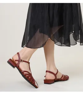 Close-up of wine red woven strap low-heel Roman sandals worn with a black pleated skirt