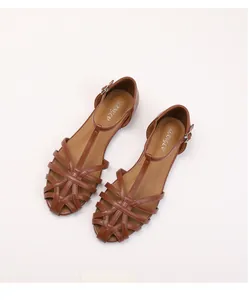 Detail of brown woven hollow-out flat Roman sandals with T-strap and buckle closure