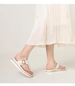 Detail of white thong sandals with gold buckle and chunky non-slip sole worn with a skirt