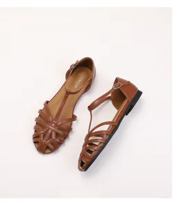 Close-up of brown woven faux leather flat sandals featuring T-strap and metal buckle