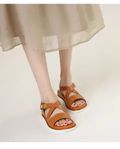 Detail view of tan cross-strap wedge sandals with gold buckle and white cushioned sole