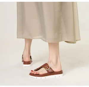Close-up of brown leather toe-post sandals with gold buckle on a white platform sole