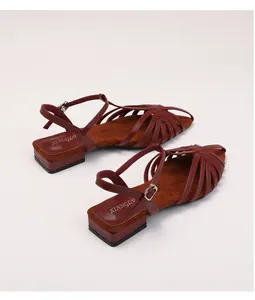 Close-up of dark red strappy flat sandals with braided texture and metal buckle detail