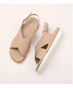 Detailed macro view of beige cross strap sandals with thick white rubber soles and gold accents