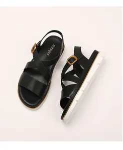 Detail of black wedge sandals with crossed straps and gold buckle on a white sole
