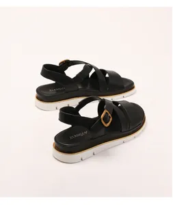 Detail view of black wedge sandals with cross straps and gold buckles on a white platform