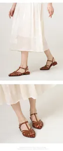 Detail of woven brown leather low-heel sandals with adjustable metal buckle strap