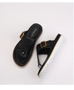 Detailed top view of black platform flip flops with a bold gold square buckle and leather finish