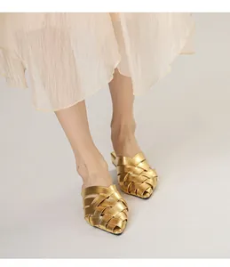 Detail view of gold woven mules with pointed toe paired with a pleated skirt