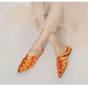 Close-up of orange metallic woven pointed-toe mule shoes worn with a beige pleated skirt