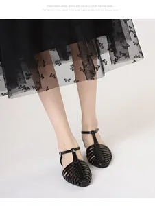 Detail of black woven T-strap roman sandals paired with a chic embroidered tulle skirt